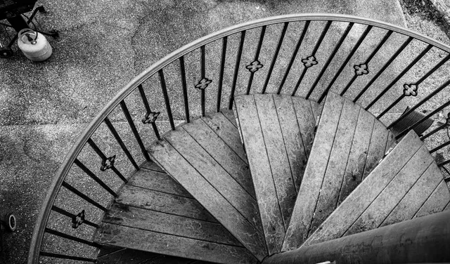 Black-and-white view looking straight down a spiral staircase with a quilted steel railing